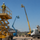 Varios tipos de plataformas elevadoras en obra con operarios con EPI trabajando.